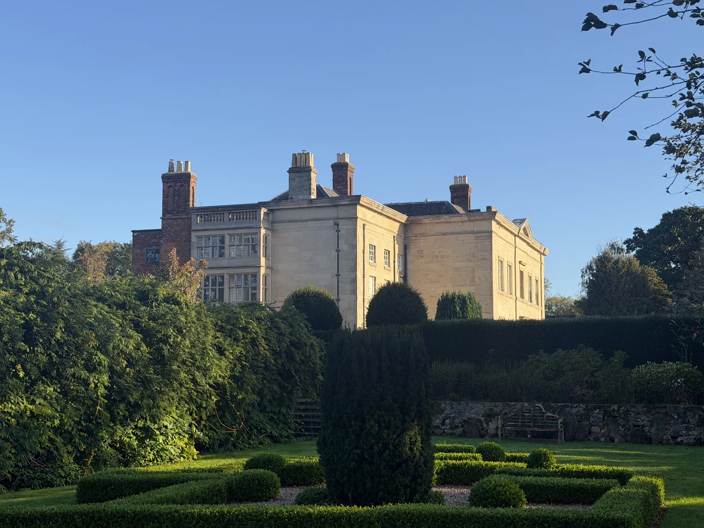 Barton Park Hall seen across the gardens and clipped yews in morning light